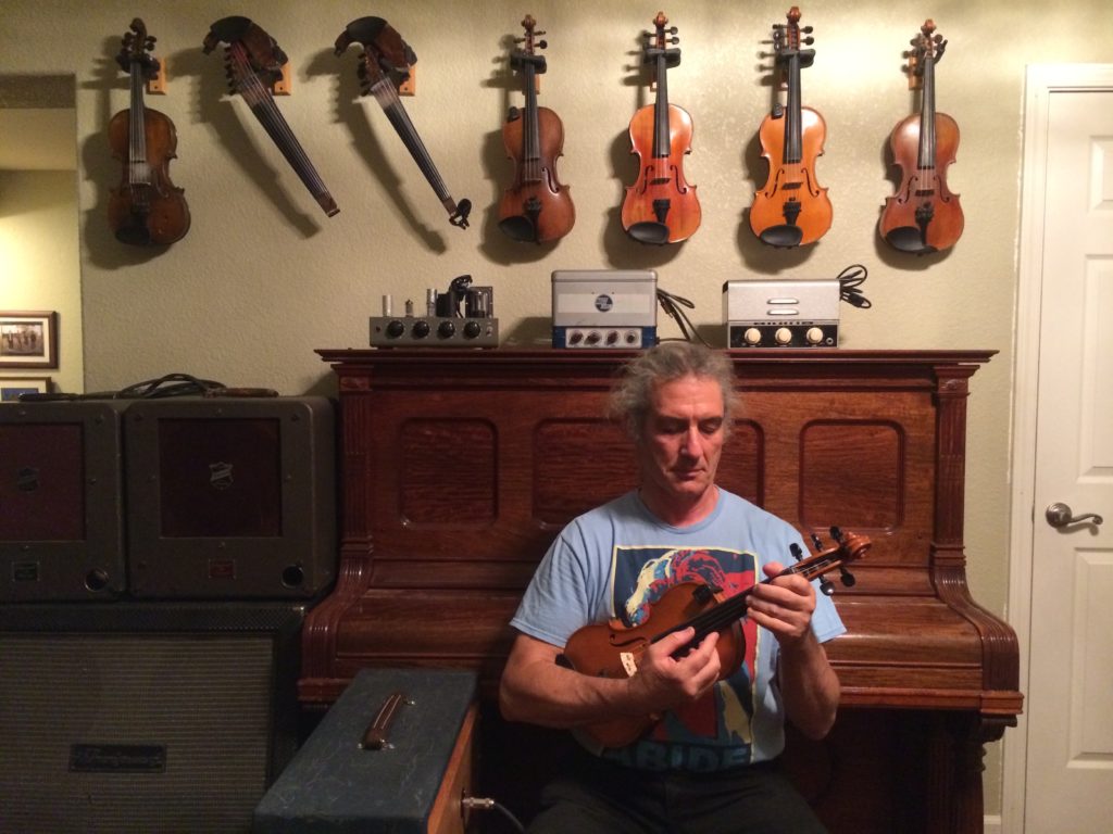 plucking violin in front of violins on the wall